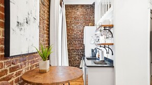 A narrow kitchen with a brick wall, a wooden table with a potted plant, and white cabinets.