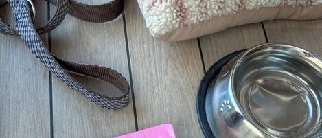A wooden table with two bags of dog food, a water bowl, and a leash.