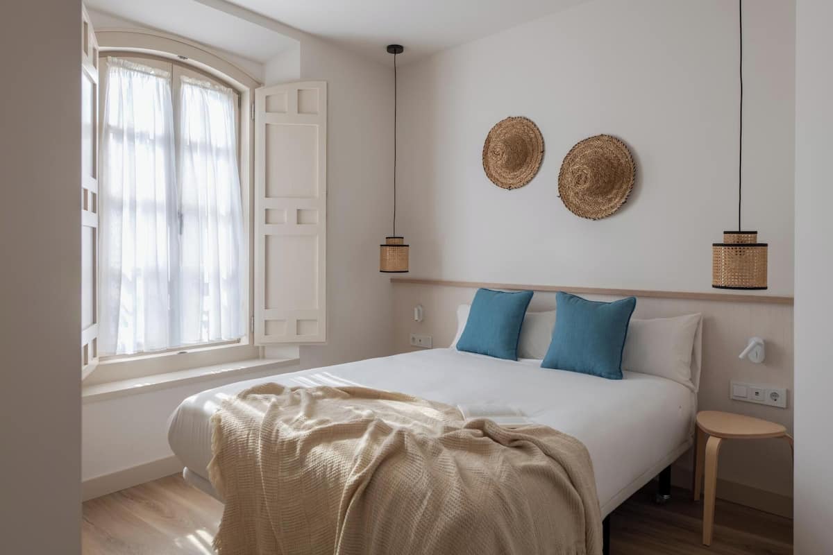 Ein Schlafzimmer mit einem Bett, einem Nachttisch, einem Fenster mit Vorhängen und zwei Wandlampen.
