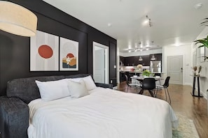 A modern bedroom with a large bed, a dining area, and a kitchen.