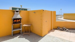 Un espace barbecue extérieur avec un gril, une table en bois et un mur jaune.