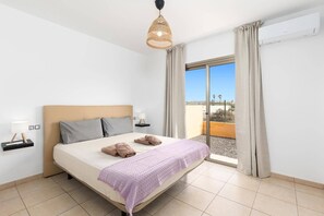 A hotel room with a bed, a bedside lamp, a window with curtains, and a view of the outdoors. - Villa Aurea House by Villa Plus (Antigua)