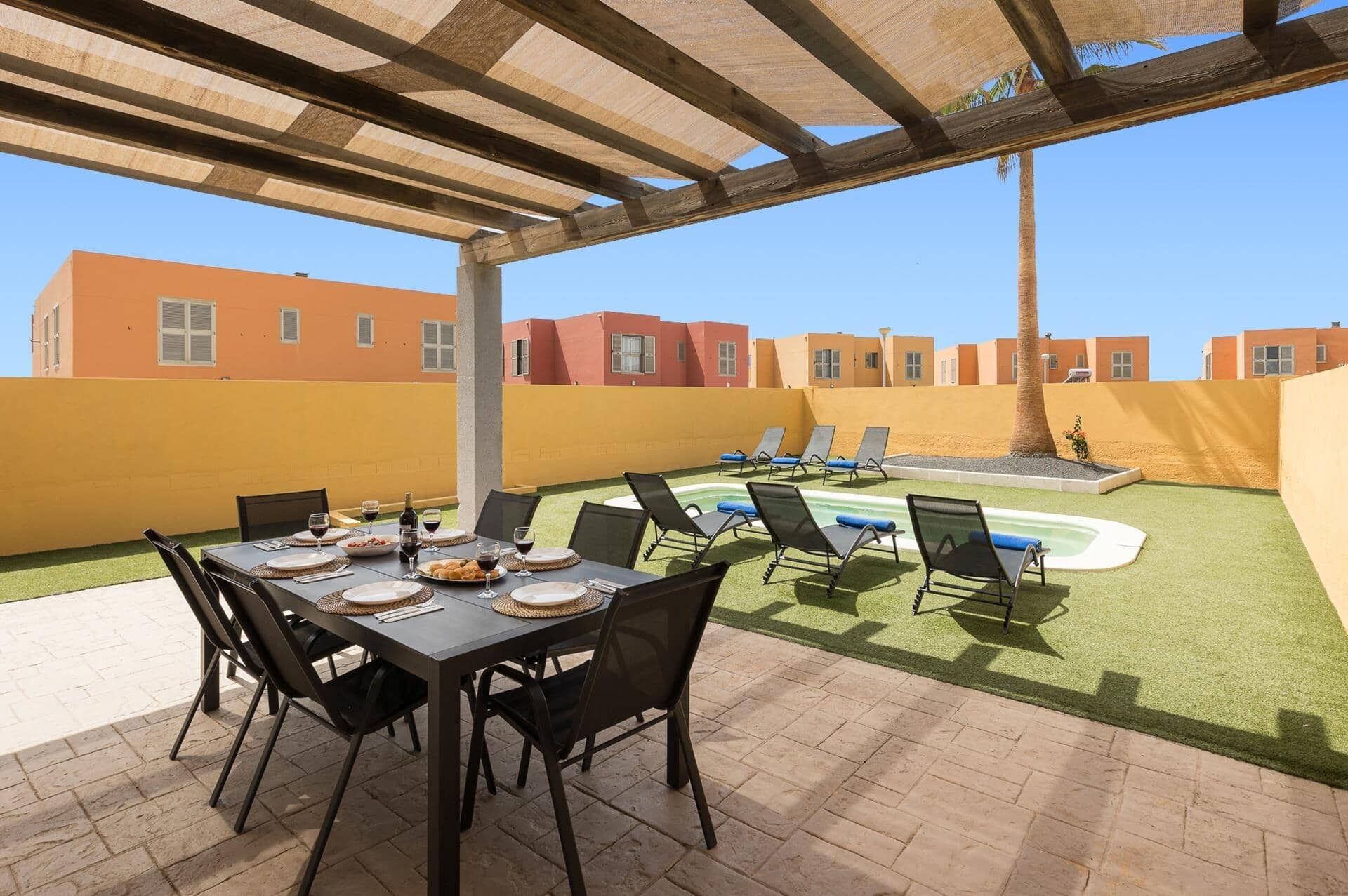 A covered outdoor dining area with a pool and lounge chairs.