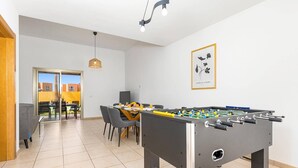 Ein moderner Innenraum mit einem Kicker, einem Essbereich mit Stühlen und einem Tisch sowie einem gerahmten Kunstwerk an der Wand.