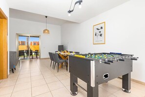Un espai interior modern amb una taula de futbolí, una zona de menjador amb cadires i taula, i una obra d'art emmarcada a la paret.