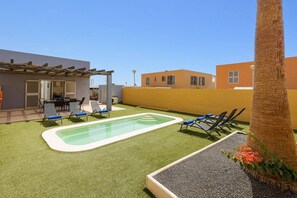 Zona de piscina al terrat amb gespa artificial, gandules i una pèrgola.