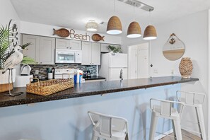 Eine moderne Küche mit weißen Schränken, einer Granitabdeckung und einer Bar mit weißen Hocker.