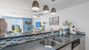 A modern kitchen with a granite countertop, stainless steel sink, and pendant lights. - Tradewinds Condominium #28- At the Beach! (Miramar Beach)