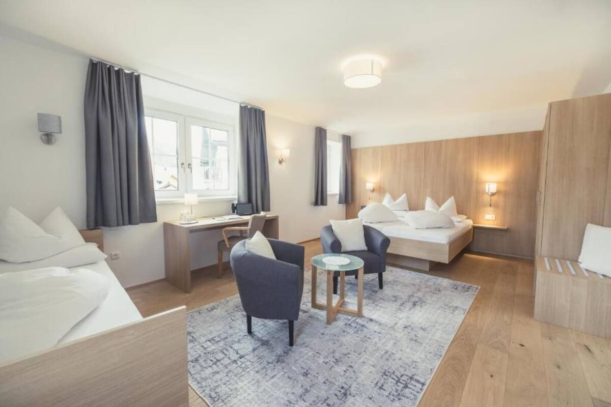 A modern hotel room with a bed, two armchairs, a desk, and a small table.