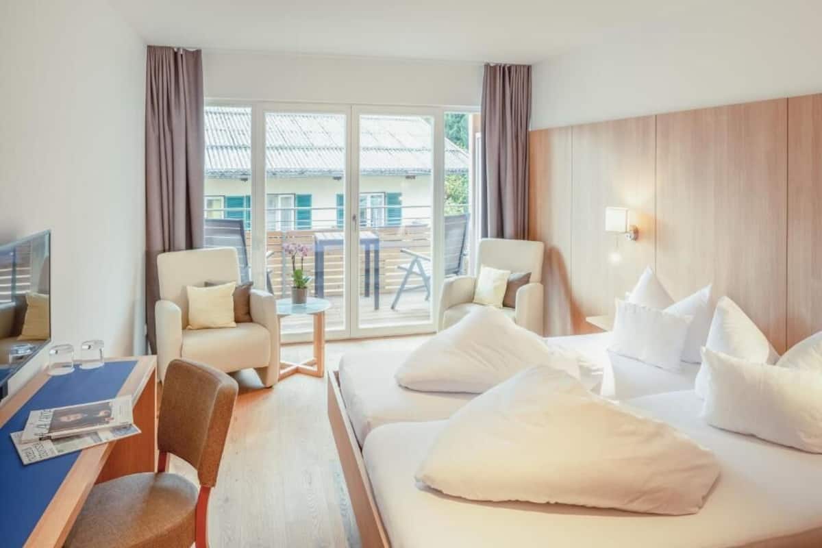 A hotel room with a bed, two chairs, a table with a magazine, and a view of the outside.