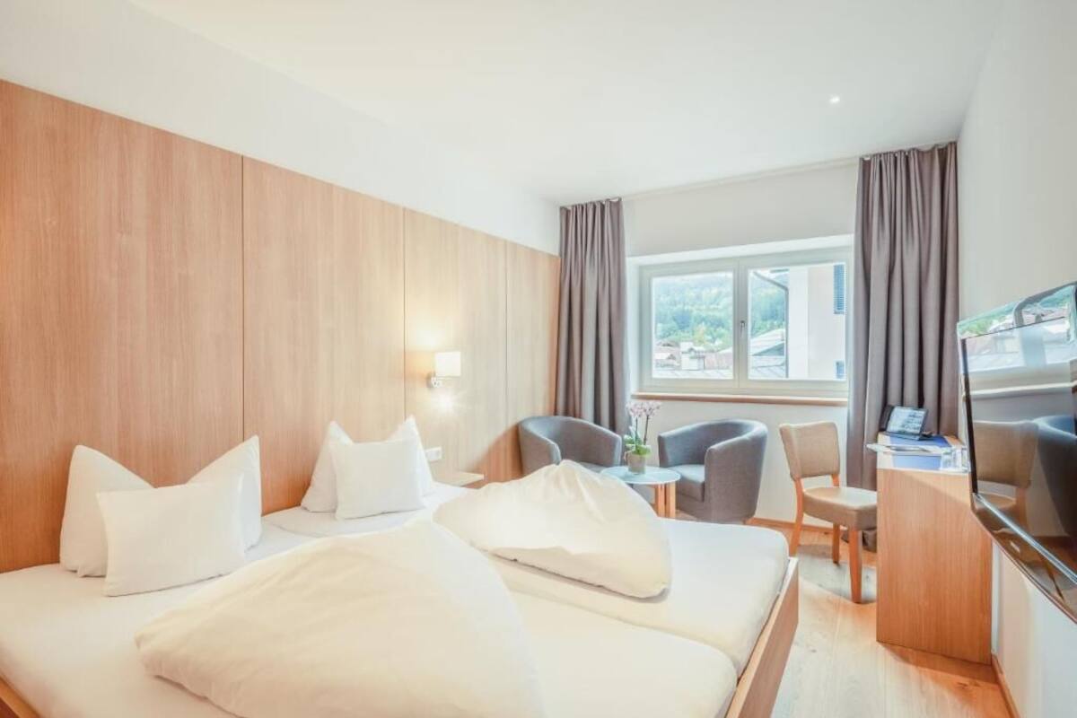 A hotel room with two beds, a desk, a chair, and a TV.