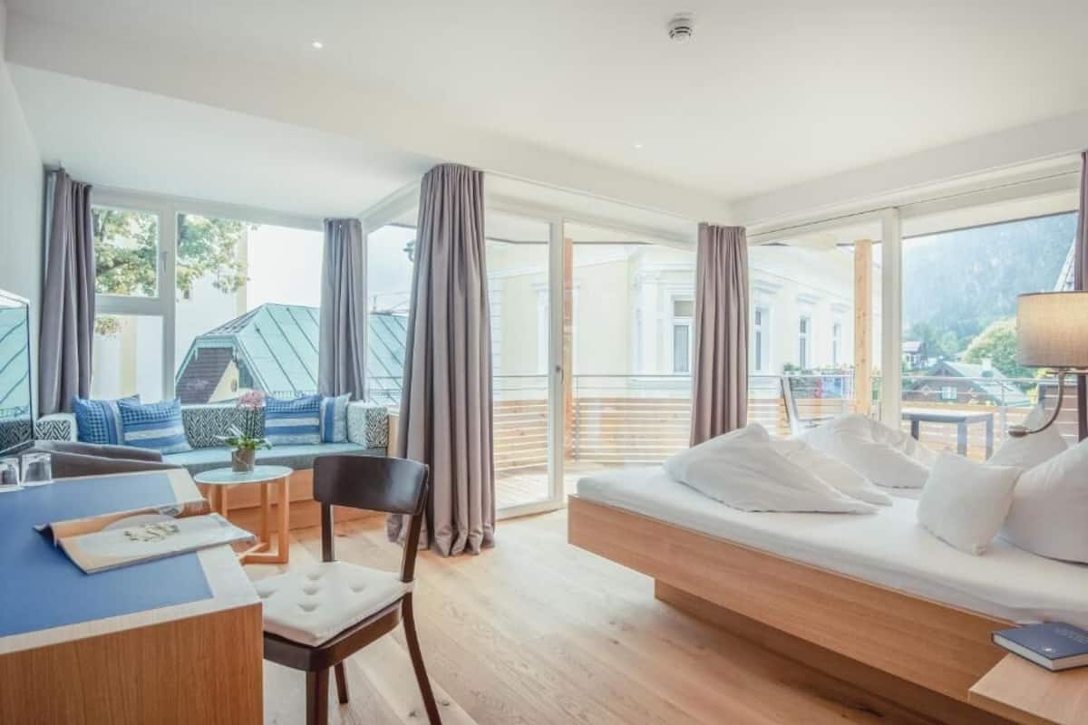 A modern hotel room with a large bed, a desk, and a seating area with a view of the outside.