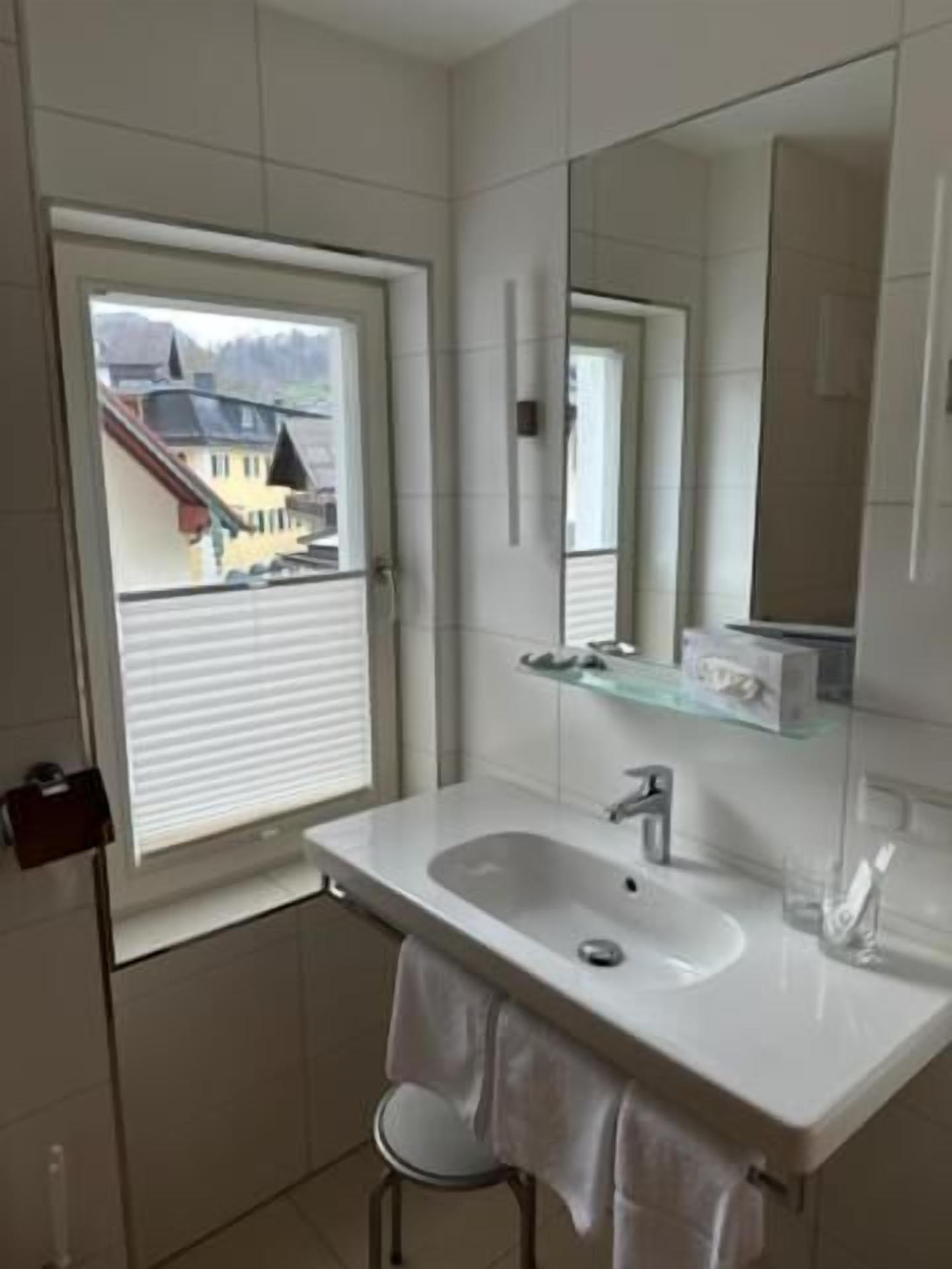 A bathroom with a window, a sink, a mirror, and a towel rack.