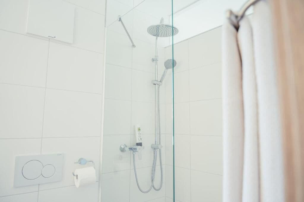 A modern shower with a glass door, a handheld showerhead, and a wall-mounted control panel.