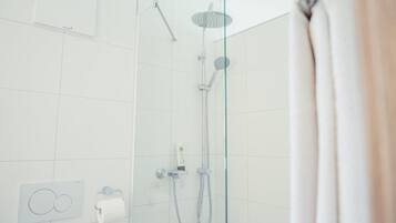 Une douche moderne dotée d’une porte en verre, d’un pommeau de douche à main et d’un panneau de commande fixé au mur.