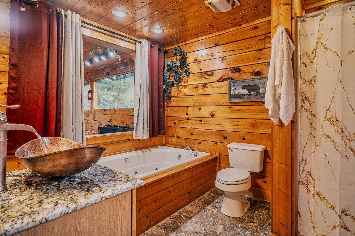A wooden cabin bathroom with a bathtub, toilet, and granite countertop.