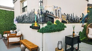 Een kamer met een stadsgezichtsmural, een houten bankje, een kleine tafel en een koffieapparaat.