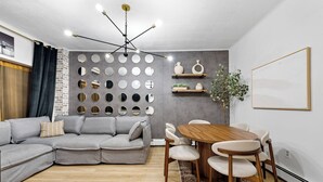 Een moderne woonkamer met een hoekbank, een houten eettafel met stoelen, een wandspiegel en een hanglamp.