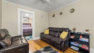 A living room with a brown leather sofa, a brown leather recliner, a black and gray rug, a ceiling fan, and a bookshelf with board games.