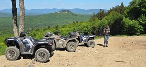 Tres vehículos todoterreno estacionados en un camino de tierra, con un paisaje montañoso y aerogeneradores al fondo.
