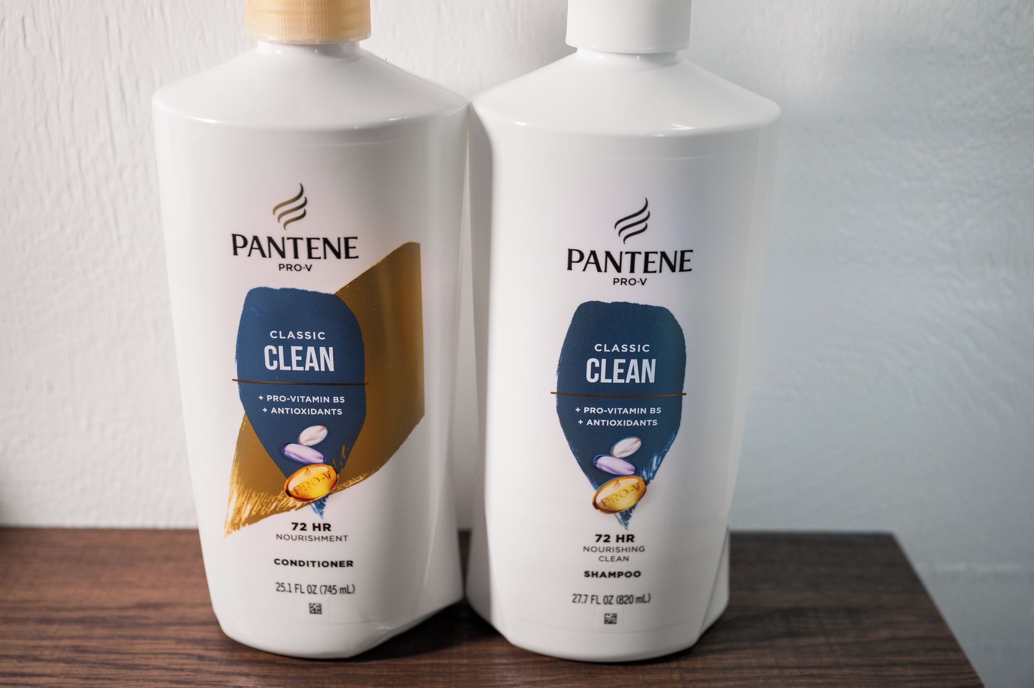 Two bottles of Pantene Pro-V Classic Clean conditioner and shampoo on a wooden surface.