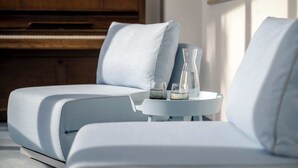 Una sala de estar moderna con un sofá, una mesita con vasos y una vela, y un piano al fondo.