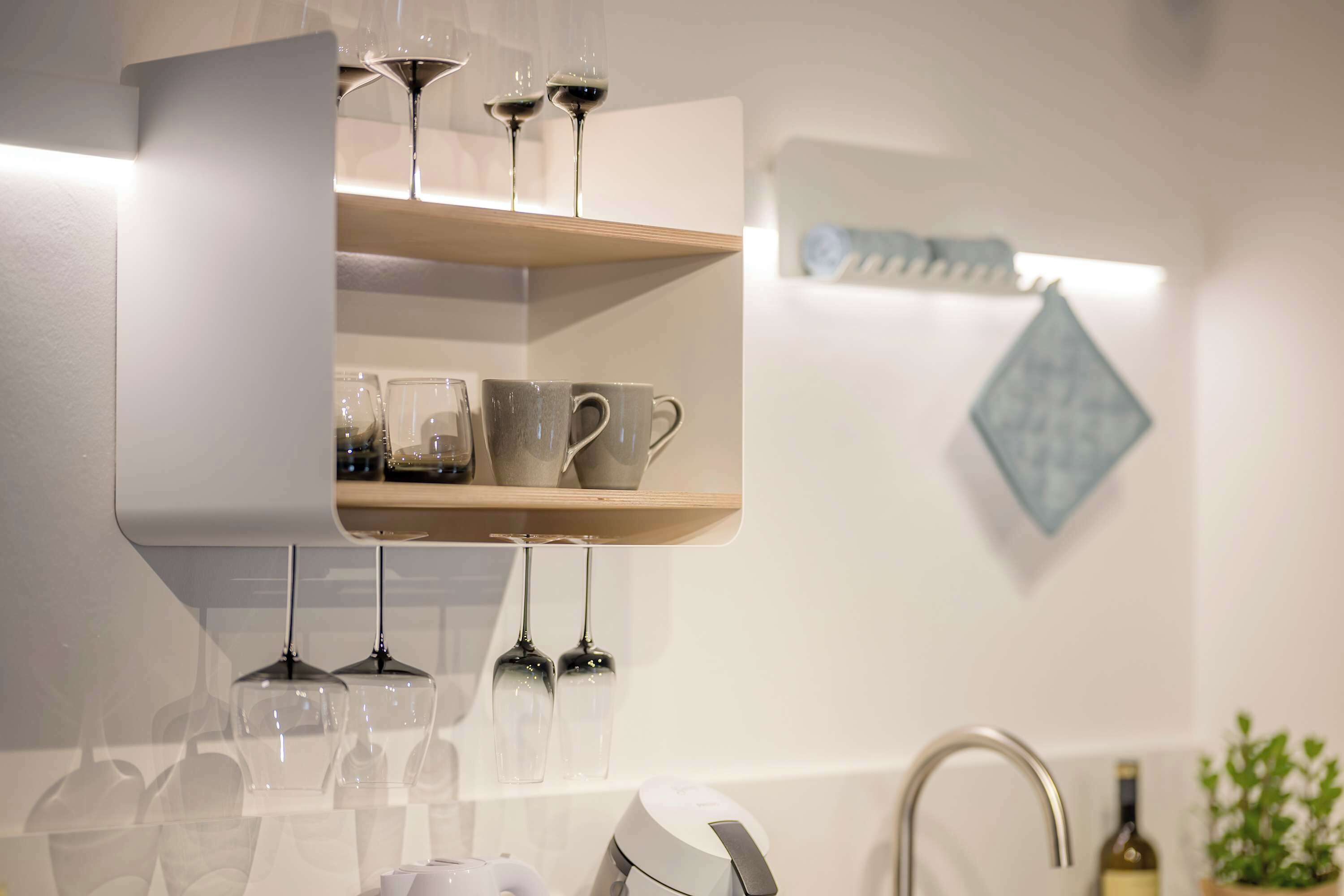A modern bathroom with a built-in shelf holding wine glasses and cups, a sink, and a decorative wall piece.