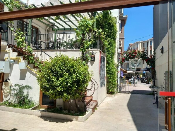 A narrow urban street with a building featuring a small garden and outdoor seating area. - DAFFNE PANSİYON (Canakkale)