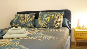 A bed with a leaf-patterned bedspread, a bedside table with a lamp, and a window with a view. - Just 50 meters from the Marines de Cogolin beach! (Cogolin)