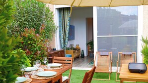 An outdoor dining area with wooden tables and chairs, a small garden, and a sliding glass door leading to a living room. - Just 50 meters from the Marines de Cogolin beach! (Cogolin)