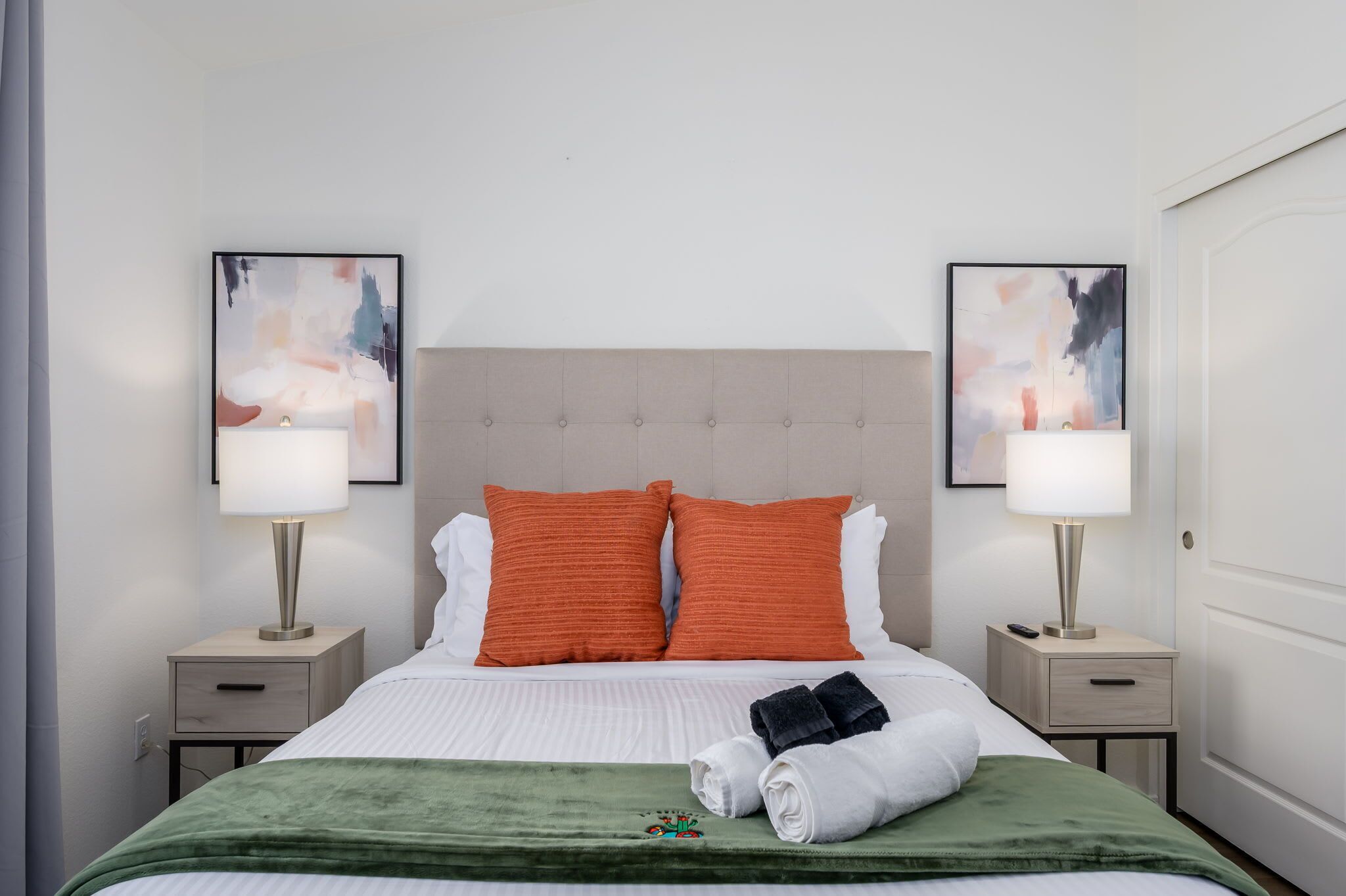 A hotel room with a bed, two nightstands, two lamps, two pillows, a green throw blanket, and two towels.