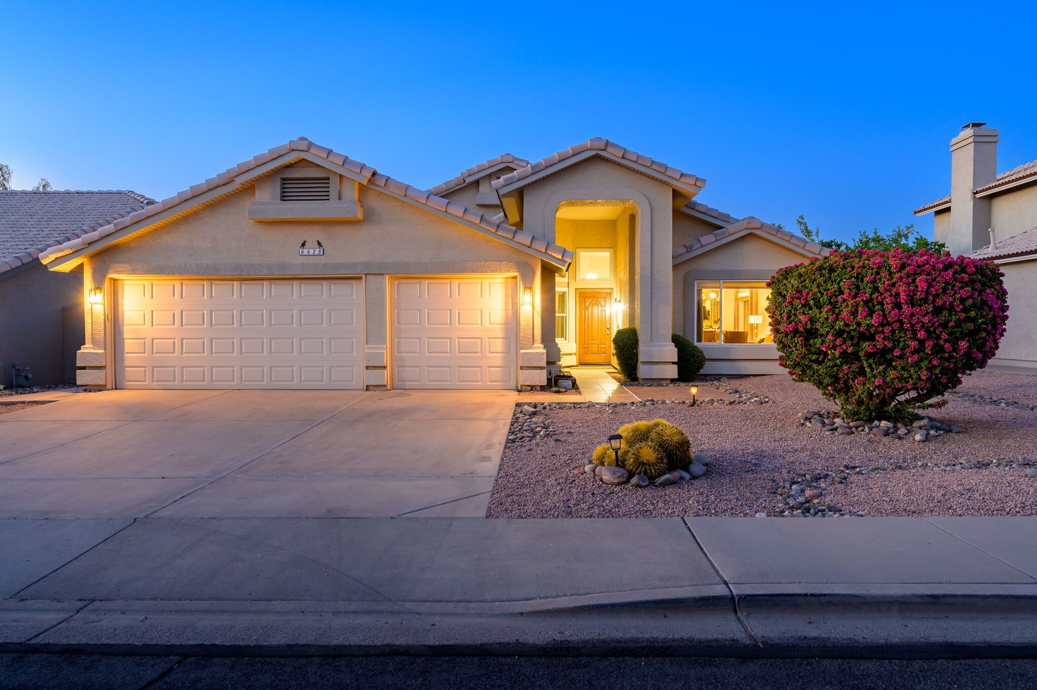 A residential house with a garage, driveway, and a well-maintained front yard with a bush.