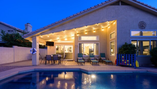 Una piscina con un porche techado, mobiliario exterior y vista al interior.