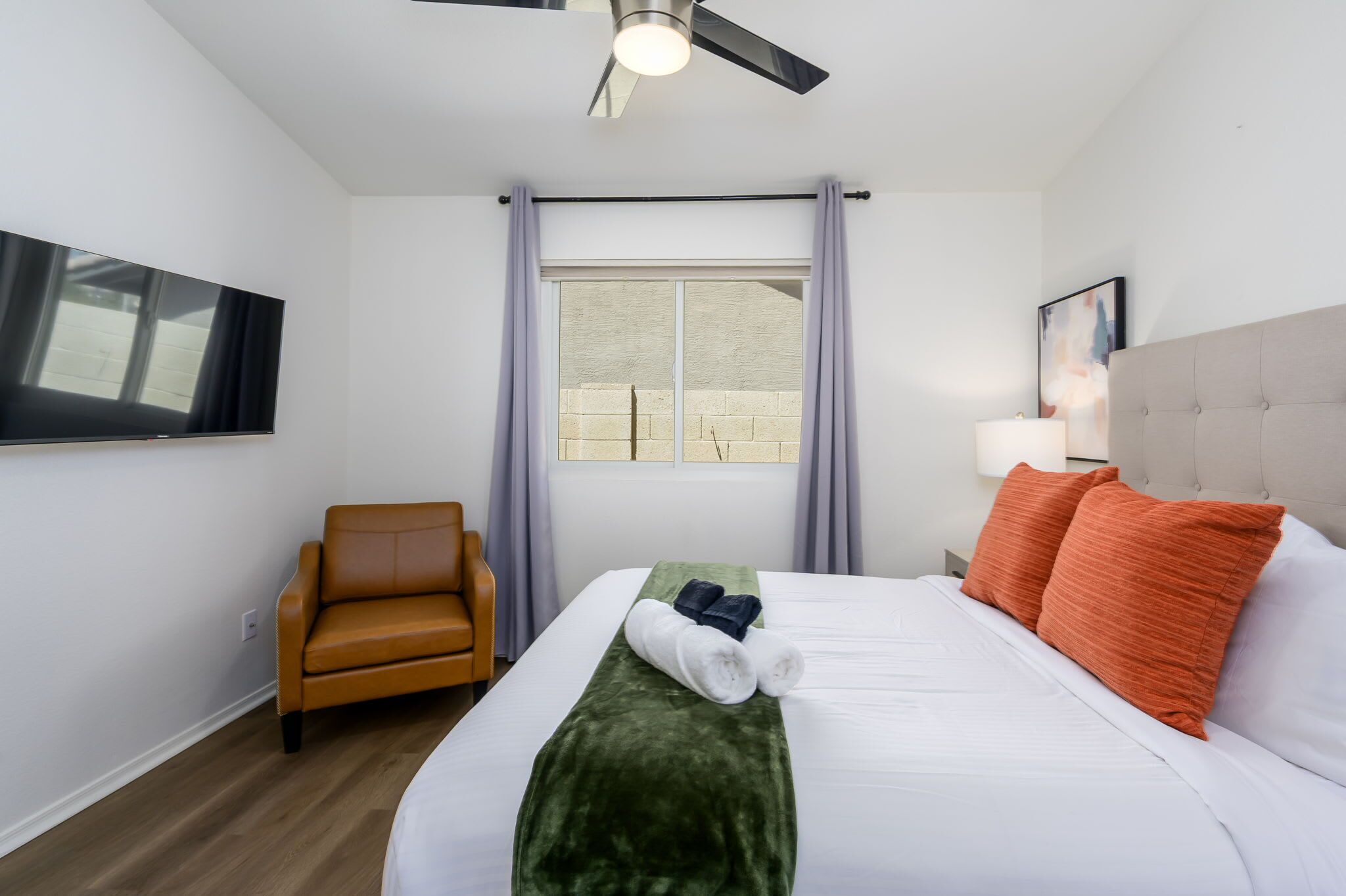 A hotel room with a bed, a chair, a TV, a window with curtains, and a ceiling fan.