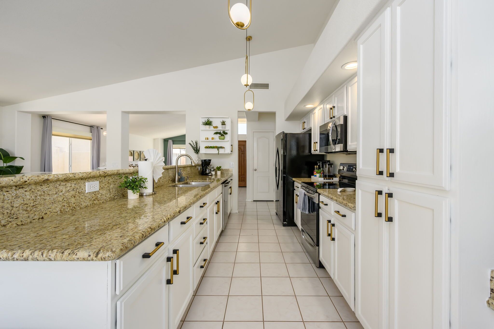 Een moderne keuken met granieten aanrechtbladen, witte kastjes en gouden knoppen.