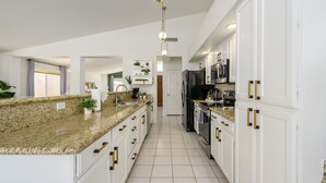 Una cocina moderna con encimeras de granito, armarios blancos y tiradores dorados.
