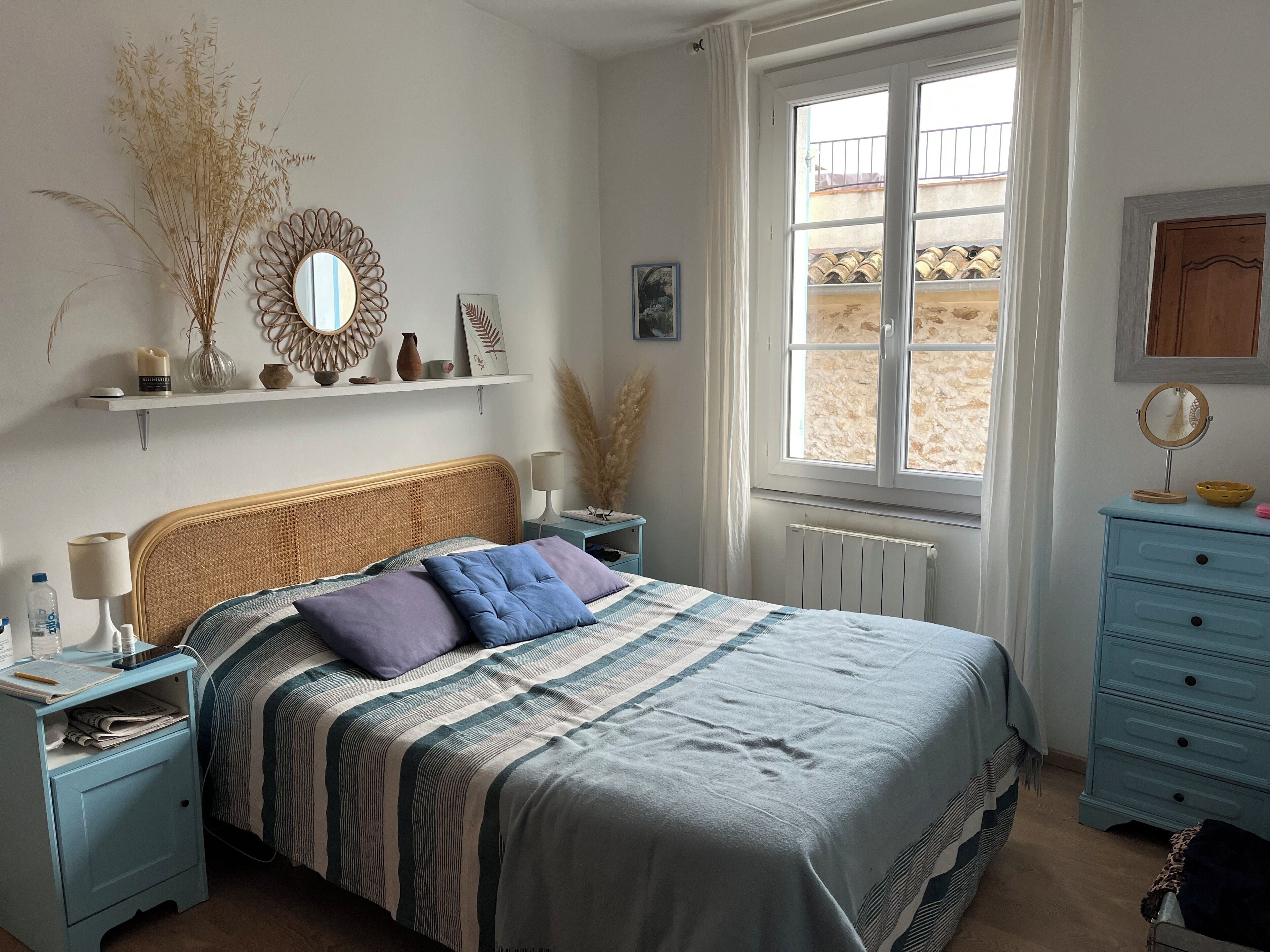 Ein Schlafzimmer mit einem Bett, Nachttischen, einer Kommode, einem Fenster und Wanddekoration.