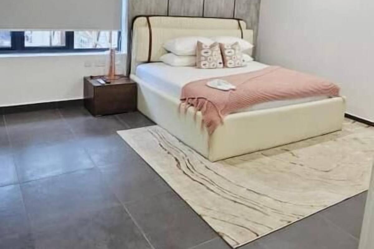 A modern bedroom with a bed, a nightstand, a window, and a wooden panel wall.