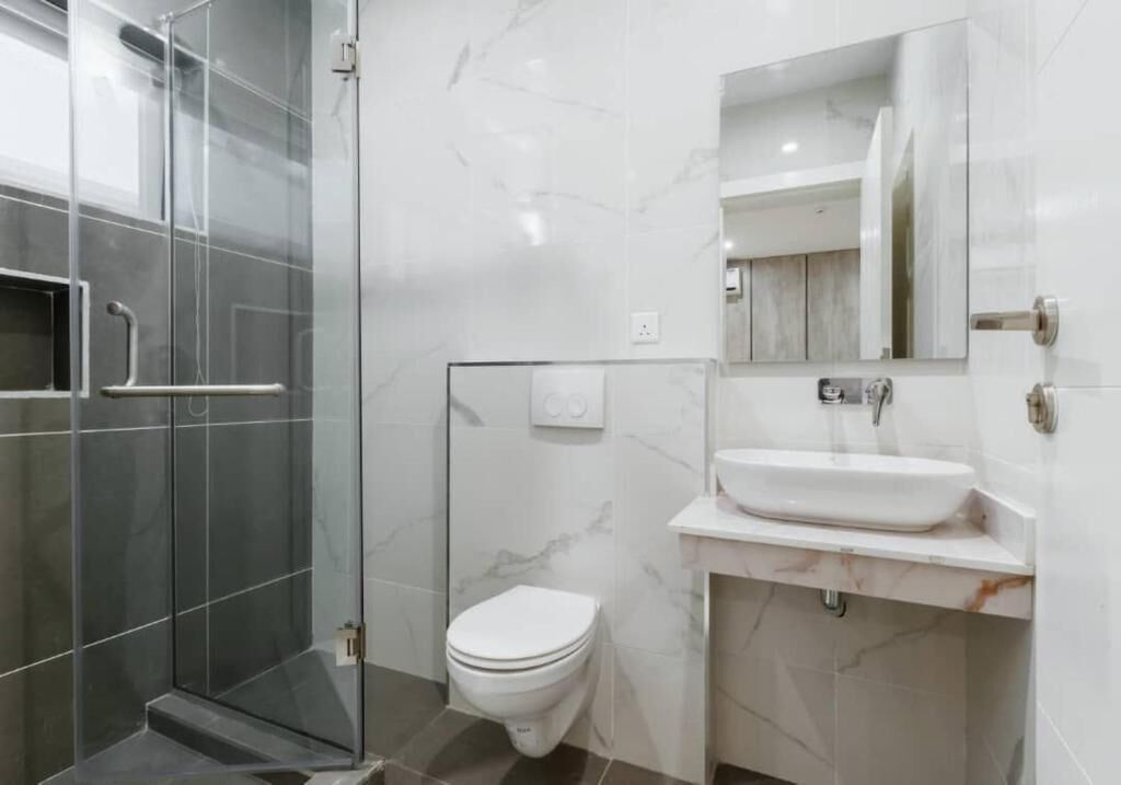 Ein modernes Badezimmer mit einer Duschkabine aus Glas, einer weißen Toilette und einem Waschbeckenbereich mit Marmorfliesen.
