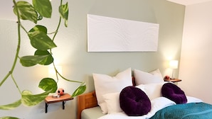 A neatly made bed with white and green bedding, a wall-mounted abstract painting, and a bedside lamp. - Immergrün Apartment – Your Relaxing Retreat with Heart & Dog in the Countryside (Stetten am kalten Markt)