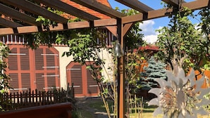 A wooden pergola with a metal bell, a brick pathway, and a wooden fence. - Immergrün Apartment – Your Relaxing Retreat with Heart & Dog in the Countryside (Stetten am kalten Markt)