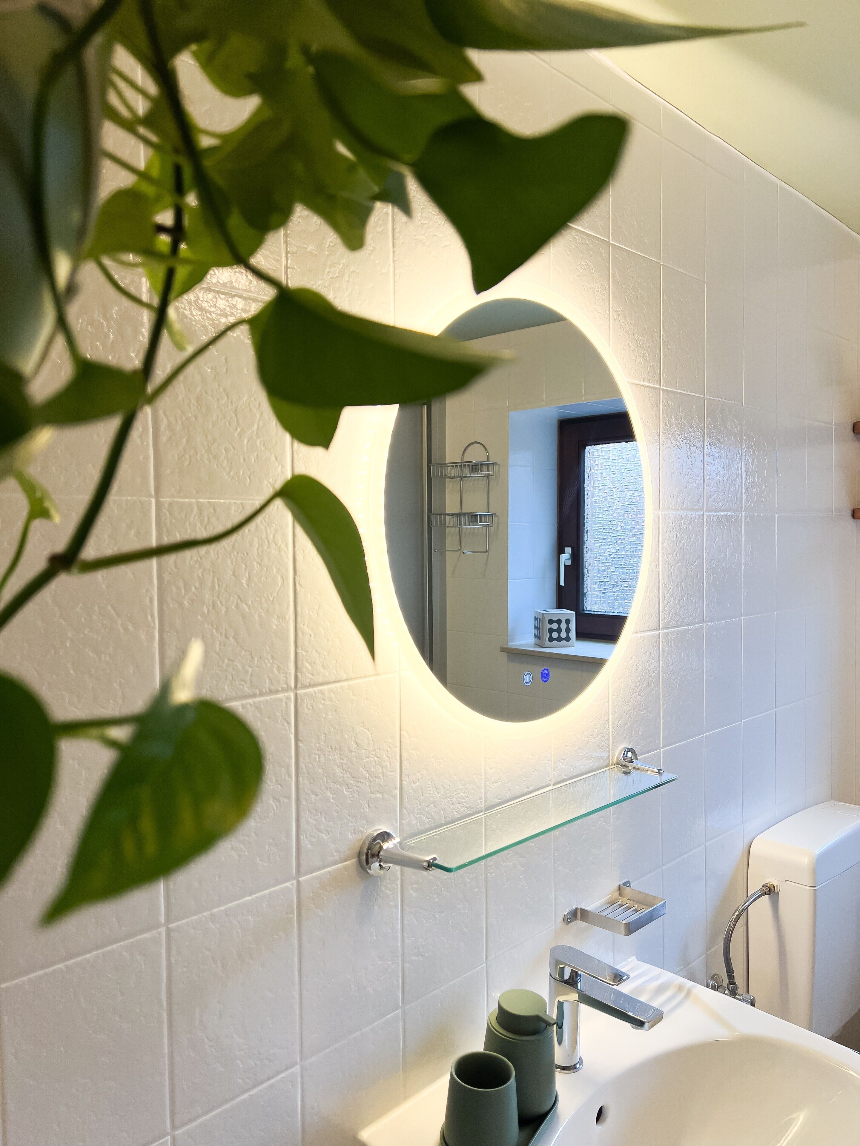 A bathroom with white tiles, a glass shelf, a sink, and a toilet.