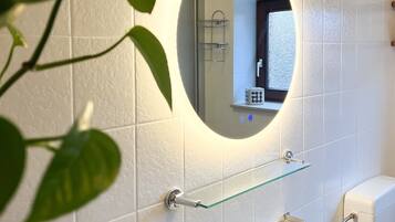 A bathroom with white tiles, a glass shelf, a sink, and a toilet.