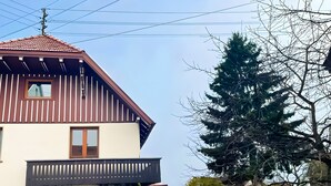 A two-story house with a balcony, a fenced yard, and a large tree. - Immergrün Apartment – Your Relaxing Retreat with Heart & Dog in the Countryside (Stetten am kalten Markt)