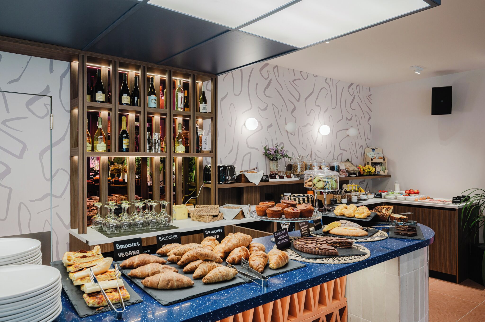 Zona de bufé con diversas opciones de comida, como cruasanes, pastelería y postres, además de una selección de vinos.
