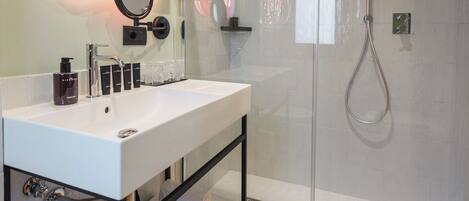 A modern bathroom with a glass shower enclosure, a white sink with a mirror, and a shelf with towels.