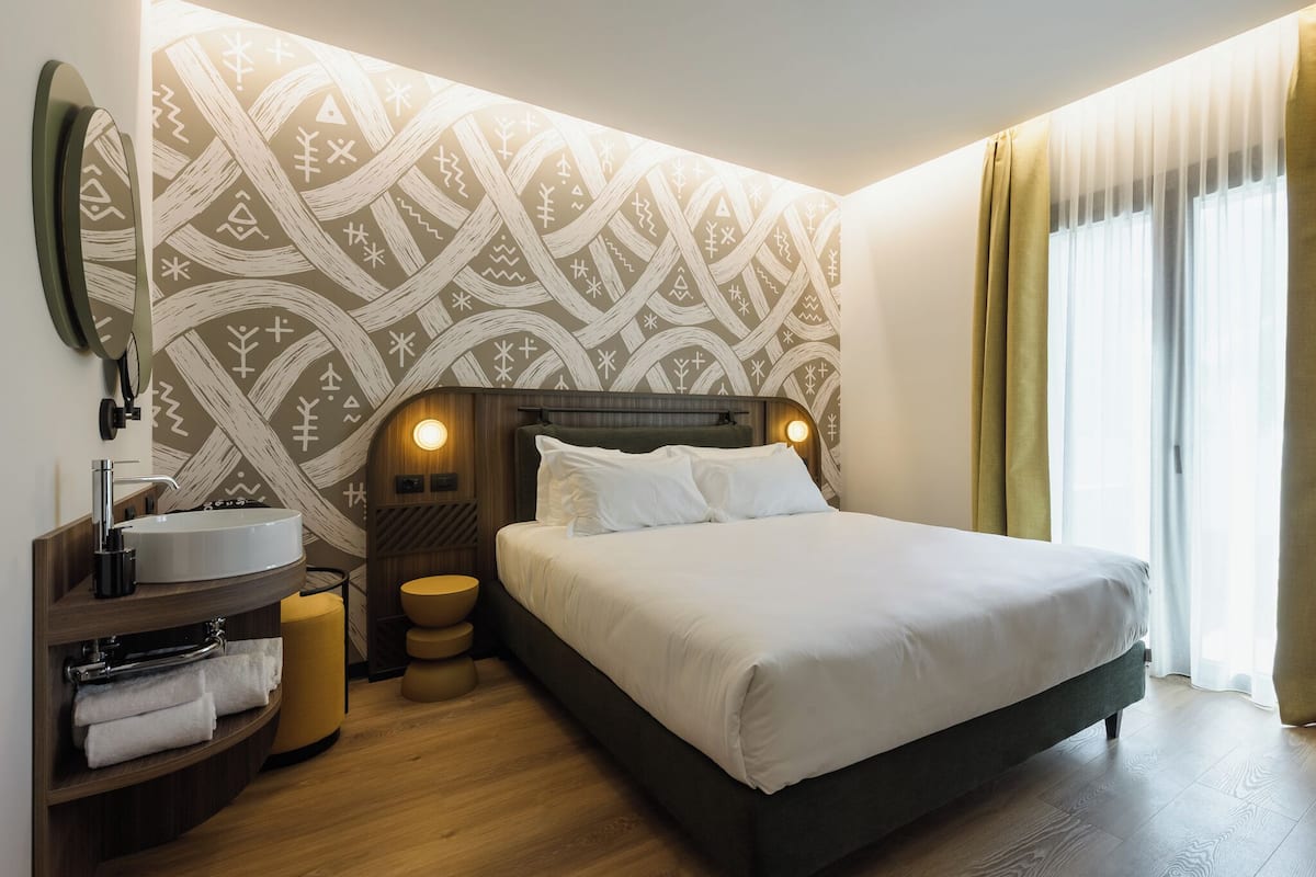 Une chambre d’hôtel moderne avec un grand lit, une table de chevet ronde, un lavabo intégré et un mur décoré d’un motif.