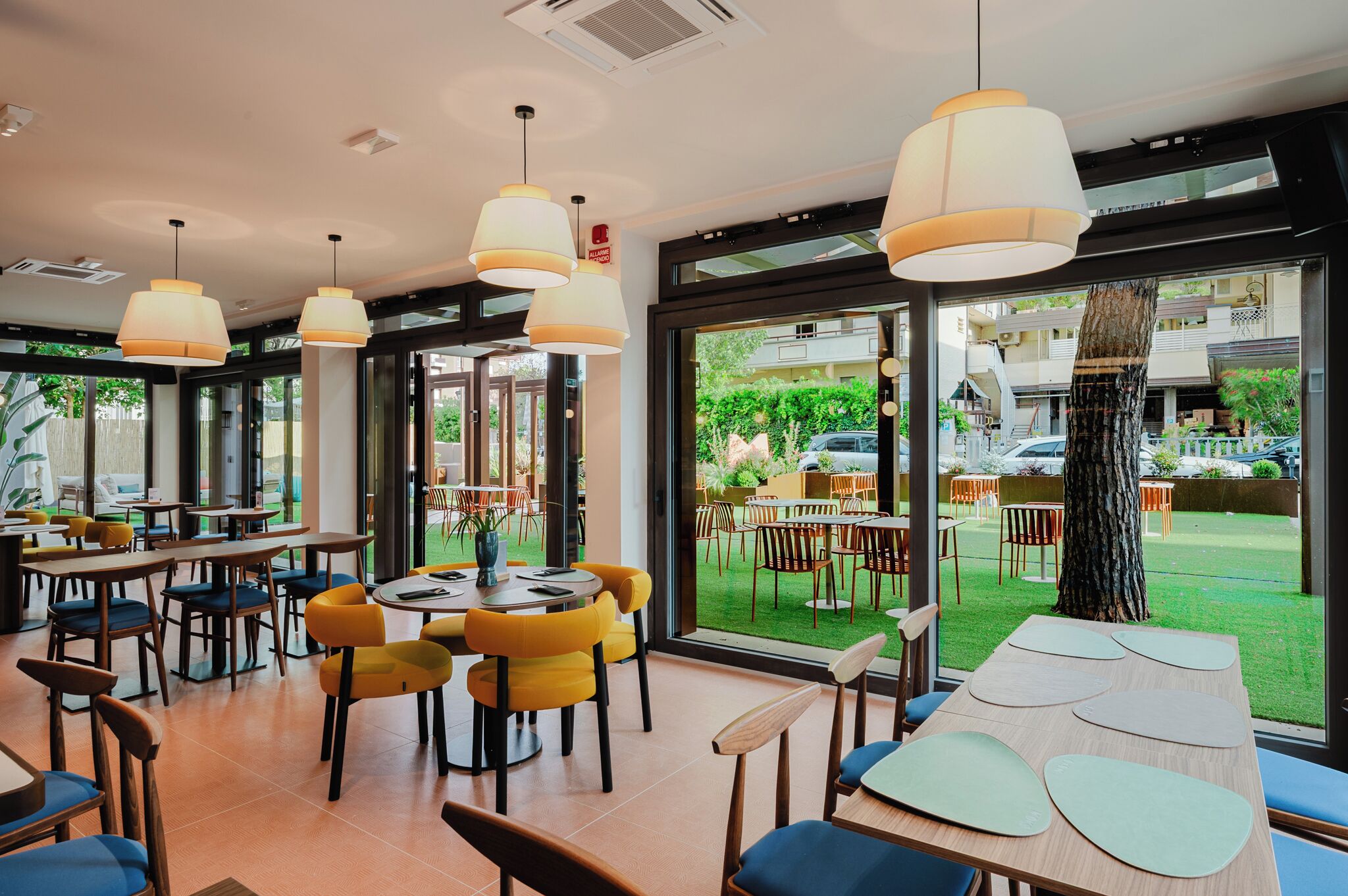A modern dining area with tables and chairs, large windows, and hanging pendant lights.