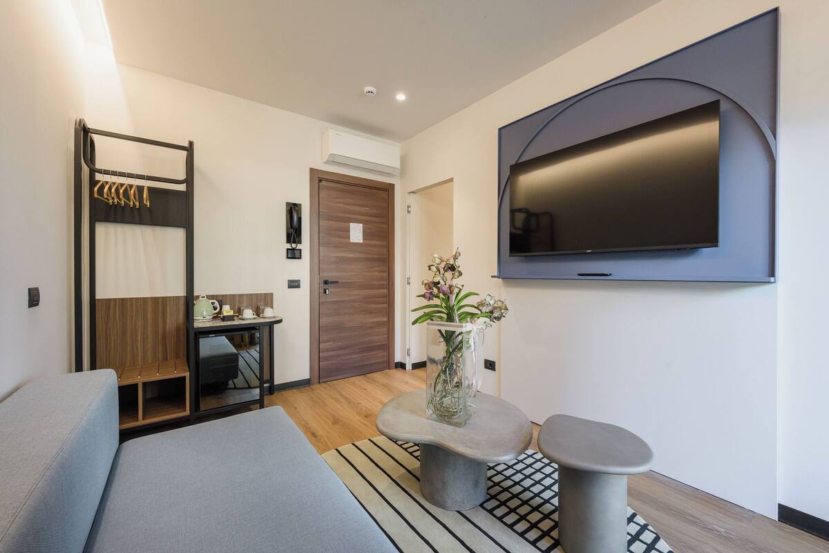 Une chambre d’hôtel moderne équipée d’un lit, d’un bureau, d’une télévision et d’une petite table sur laquelle est posé un vase.
