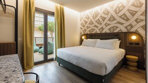 A hotel room with a bed, a desk, a chair, a window with curtains, and a patterned wall.